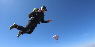 Skydiver in freefall with an open parachute in the background